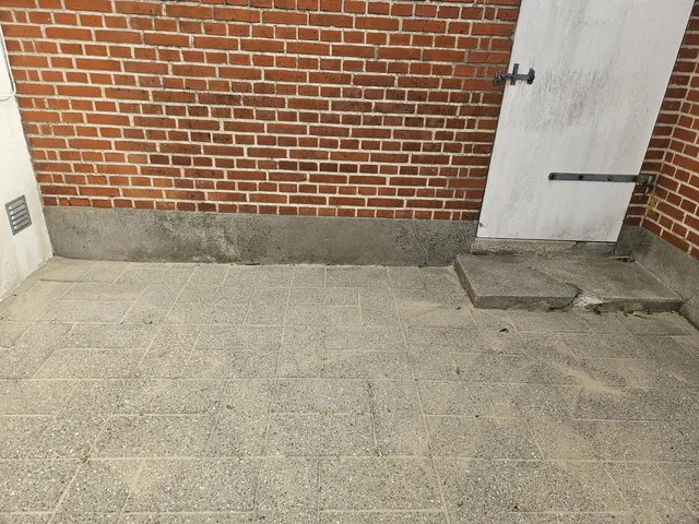 Efter fliserens: de samme fliser i gårdhaven er lyse og rene foran den røde murstensvæg og den hvide dør.