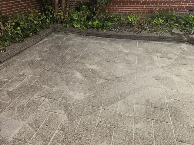 Efter fliserens: den samme terrasse med rene, lysegrå fliser og tydelige fuger, set fra samme vinkel.